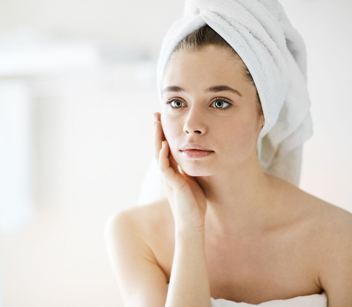 En kvinne med et håndkle i håret ser på seg selv i speilet